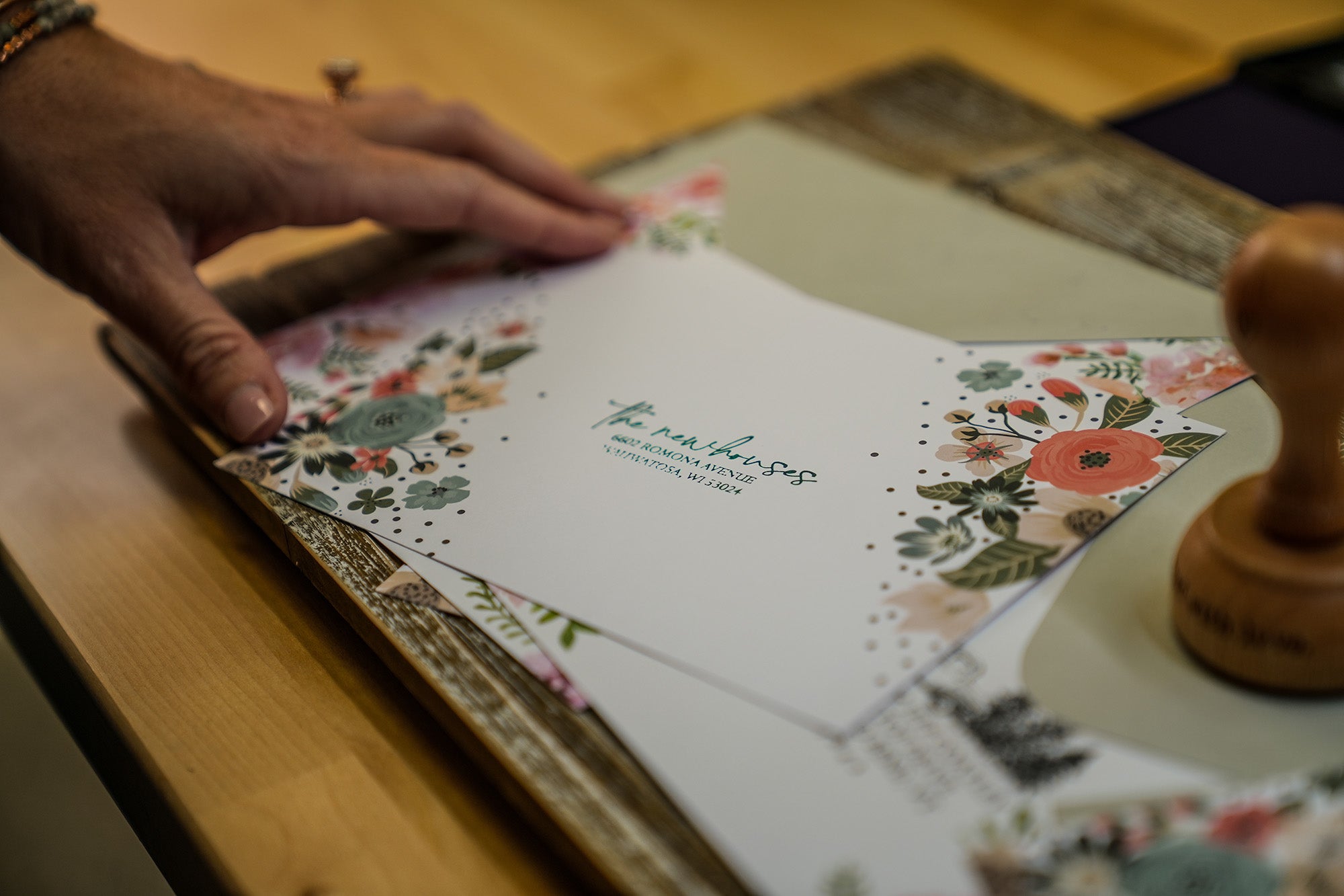 Hand of a person carefully preparing a decorative paper with floral patterns for custom stamping with a clear focus on the paper and the stamp ready for use on the side