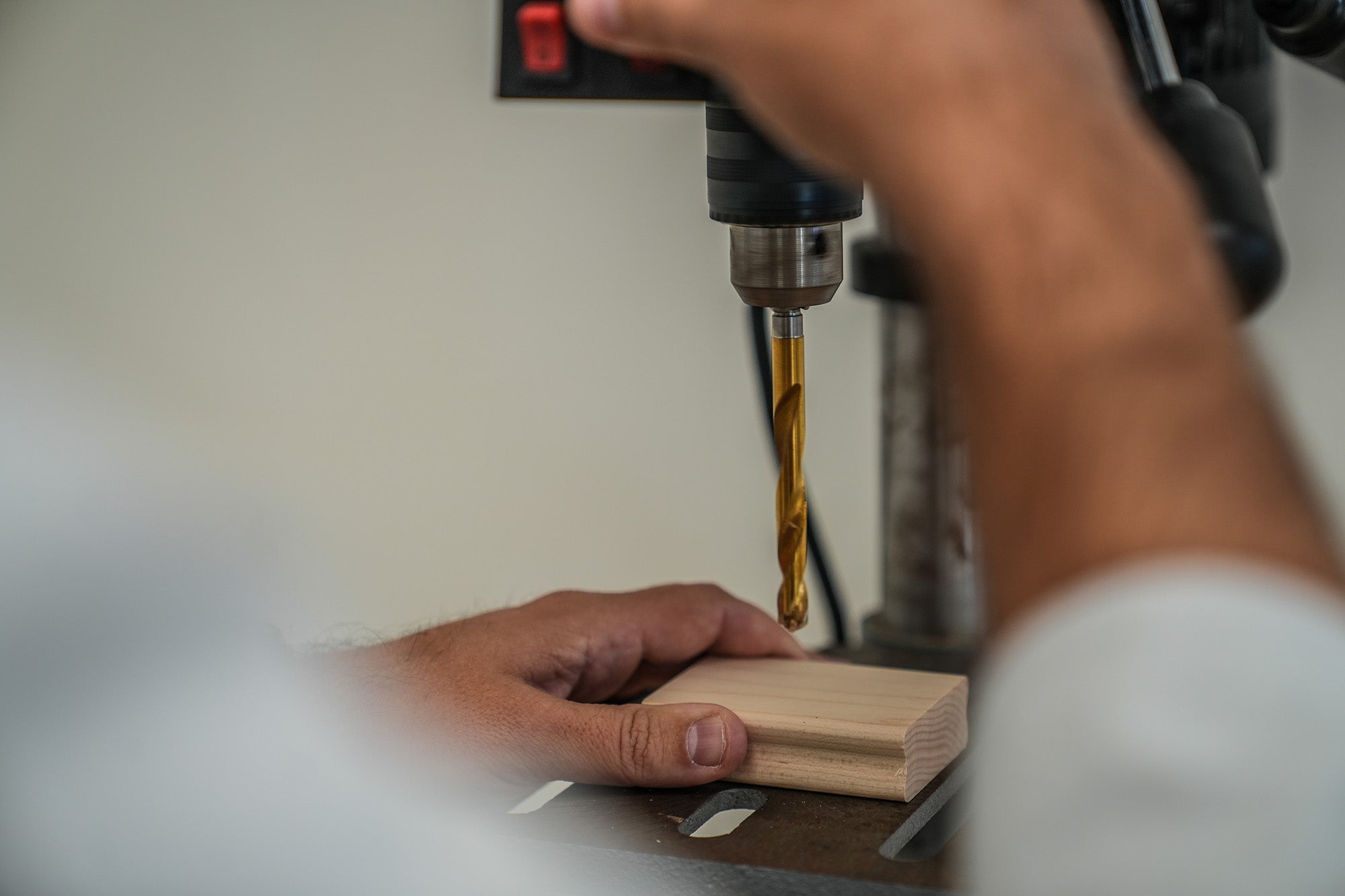 A craftsman precisely drilling into a block of wood to create a handle for a custom rubber stamp with the focus on the drill bit and the wood and the craftsman's hands guiding the process