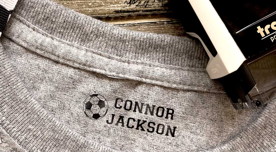 Personalized fabric name stamp with soccer ball icon and "Connor Jackson" text on gray shirt