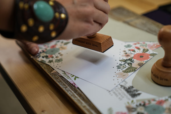 Hand holding a wooden rubber stamp above a floral stationery paper