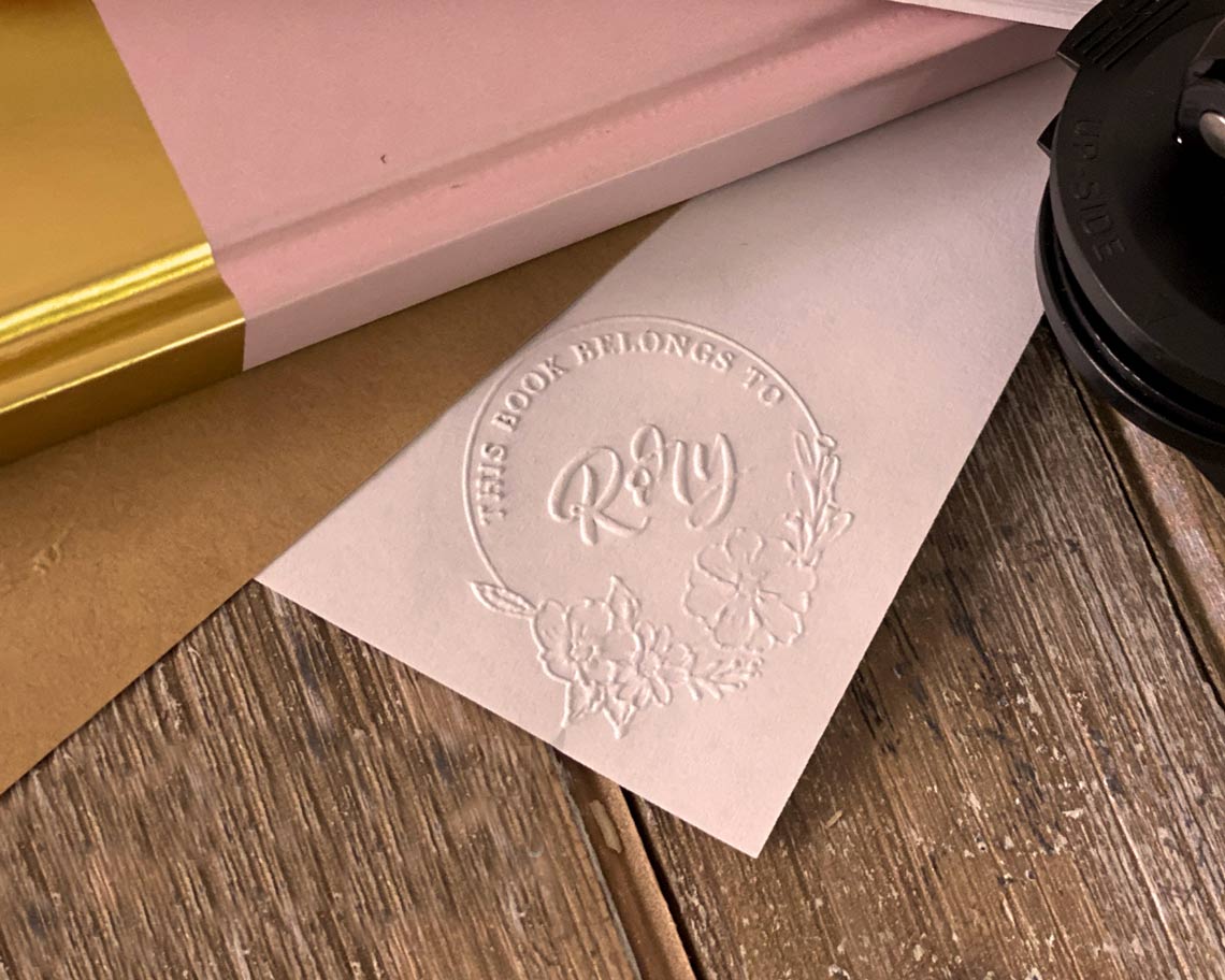 a paper embossed with custom personal library embosser that says this book belongs to and the owners initials