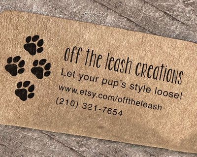 A custom rubber stamp imprint on a business card for Off the Leash Creations with paw prints and contact information on a textured background