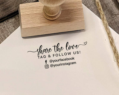 A white paper with Share the Love Tag & Follow Us and social media handles stamped on it with a wooden rubber stamp and twine on a textured surface