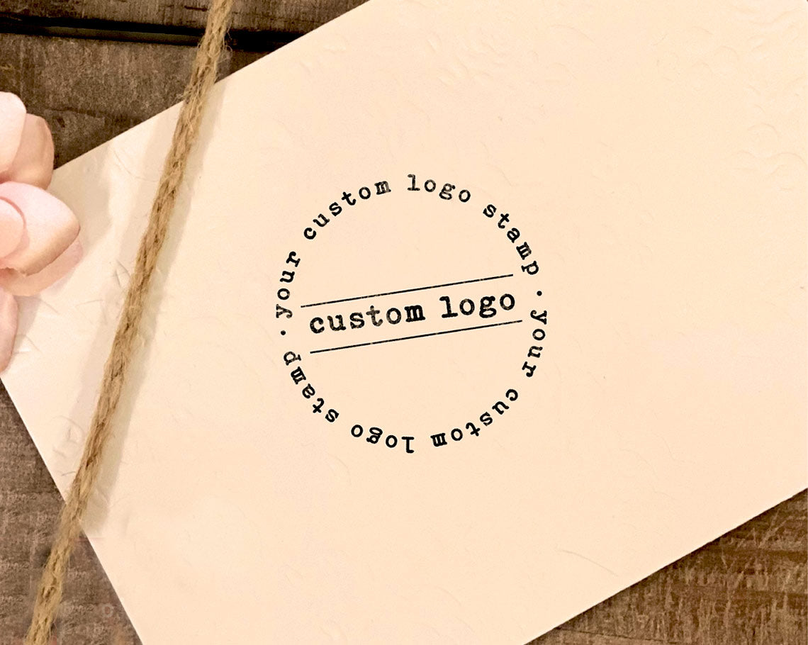 Circular rubber stamp imprint with the text YOUR CUSTOM LOGO STAMP on beige paper, with a twine bow on the side.