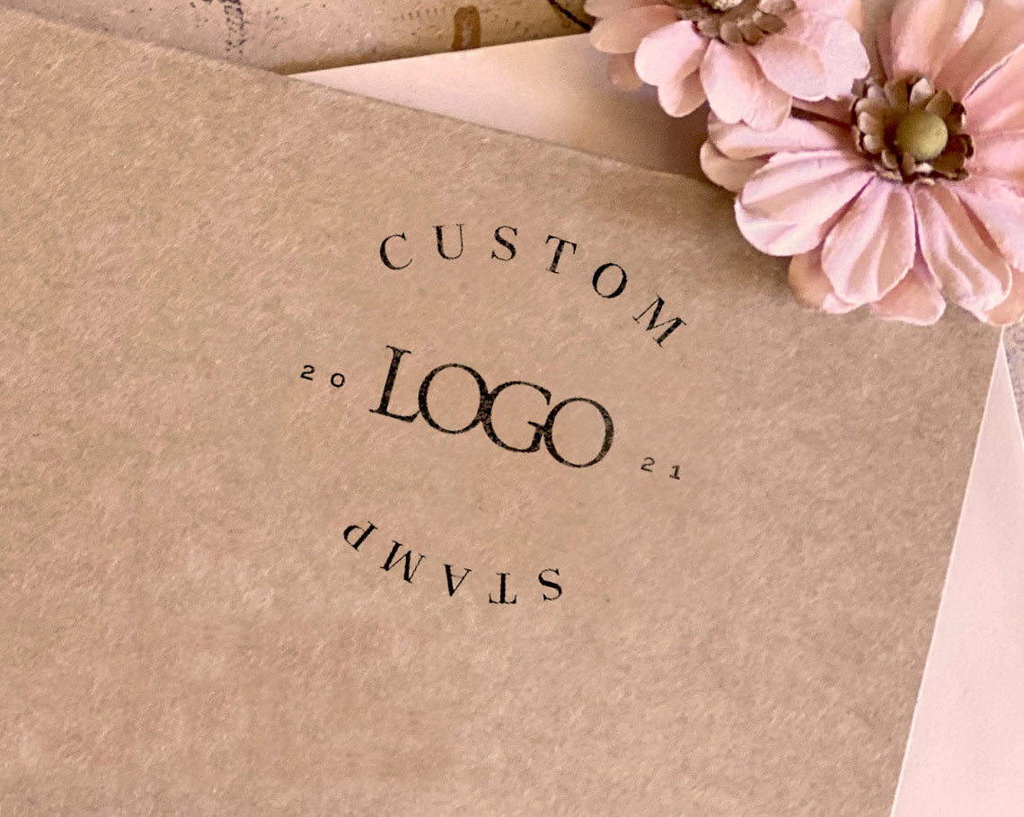 self inking stamp imprint of CUSTOM LOGO with the year 2021 arranged in a circle on brown paper, accompanied by a pink paper flower.