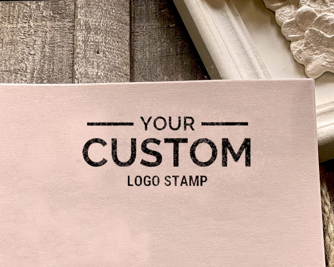 business logo stamp imprint reading YOUR CUSTOM LOGO STAMP on pale pink paper against a wooden backdrop.