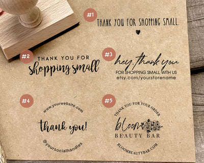 Craft paper with various thank you messages and a Bloom Beauty Bar stamp impression next to a wooden stamp handle on a wooden background